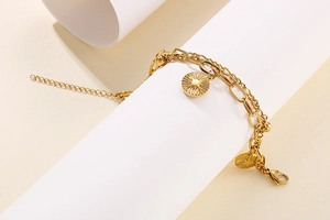 Detail of gold double-layer chain bracelet featuring a sunburst coin pendant