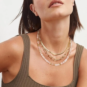 Macro detail of layered gold snake chain, thick link chain, and pink beaded necklace set