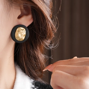 Side view of model wearing a round gold hammered texture earring with a black outer border