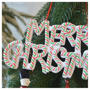 Detail of Merry Christmas letter ornament with candy cane stripe hanging on a green tree