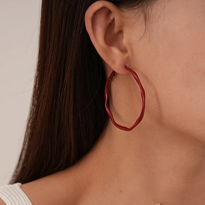 Close-up of red irregular wavy metal hoop earrings with glossy painted finish on model