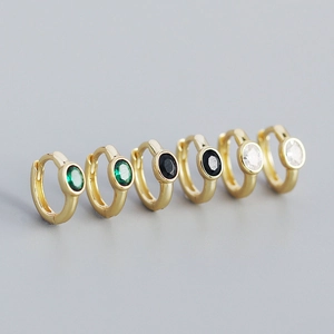 Detail of s925 silver gold-plated huggie earrings with oval emerald, black, and clear zircon