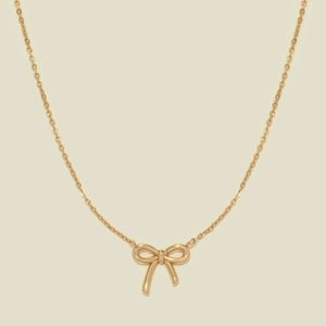 Dettaglio della collana a fiocco placcata in oro con catena a serpente su sfondo beige