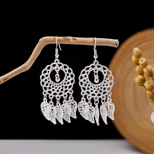Detail of silver bohemian earrings with hollow leaf tassels hanging on a wooden branch