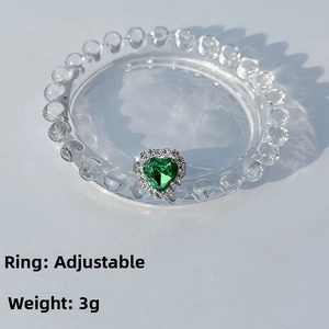 Detail of adjustable silver ring featuring a green heart gem and diamond halo