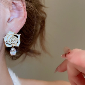 Detail view of white enamel rose earring with gold plating and teardrop zircon drop