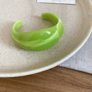 Close-up of a light green acrylic open bangle with marble texture on ceramic tray