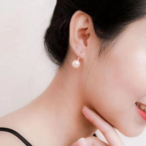 Detail view of a white round pearl earring with rose gold hook on model's ear