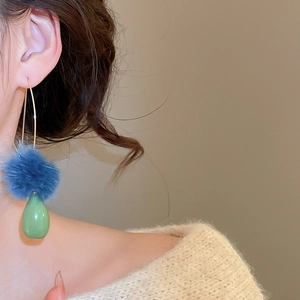 Dettaglio degli orecchini invernali con pompon blu e pendente a forma di goccia verde