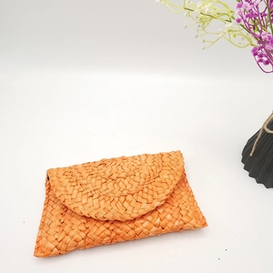 Dettaglio della pochette in paglia di mais arancione con chiusura a patta curva