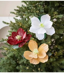 Three large glittered fabric magnolia flowers on a Christmas tree with glowing warm lights