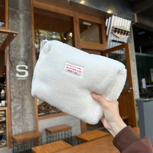 Close-up of white plush fleece makeup bag with embroidered quote label held in hand