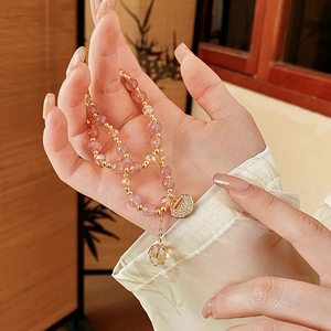 Detailed close-up of a pink strawberry quartz beaded bracelet with a gold heart lock charm