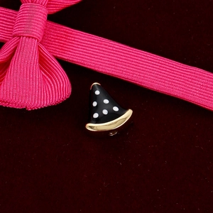 Detail of a black enamel triangle bead with white dots and gold trim on velvet
