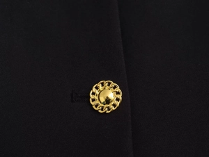 Detailed macro view of a gold relief button with chain texture on black fabric