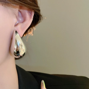 Close-up of model wearing polished silver teardrop earrings with a glossy metal finish