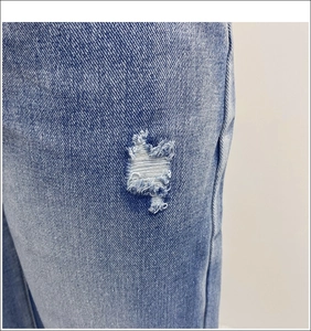 Detailed close-up of distressed ripped details on blue wide-leg denim jeans fabric