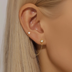 Detail of gold chain earrings featuring star charms with zircon stones on female ear