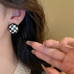 Close-up of a model wearing checkerboard patterned round earrings with silver pins