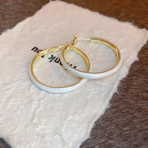 Detail of gold hoop earrings with textured white enamel coating and secure clasp closure