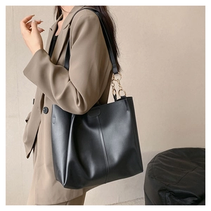 Detail view of a large black leather tote bag with gold chain strap worn by a model