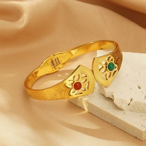 Macro shot of gold fan-shaped open cuff with red and green gems on stone and silk