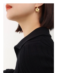 Close-up of a gold flower-shaped earring worn on model ear with 18K gold-plated finish