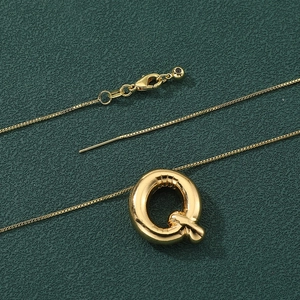 Macro shot of gold balloon style letter Q pendant necklace on dark textured background