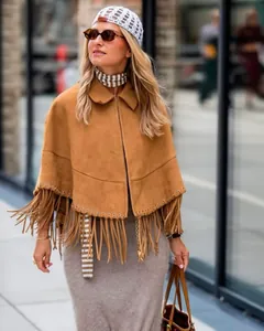 Detail of caramel brown suede poncho featuring metallic eyelets and dense tassel fringe