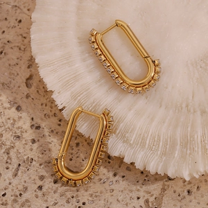 Close-up of gold U-shaped earrings with round zircon stones on a white coral stand