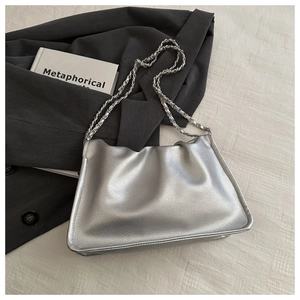 Detail of silver pleated cloud bag with metallic chain strap on minimalist background