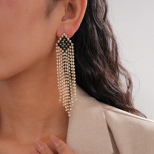 Close-up of long gold fringe earrings with black diamond shape and white rhinestones