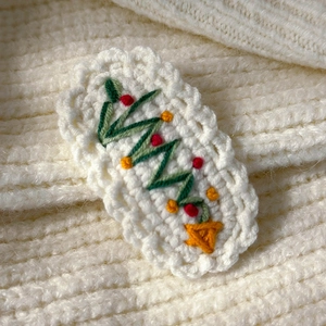 Close-up of a handmade crochet Christmas tree hair clip on a white knitted background