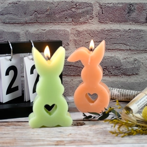 Detail of bunny candles with heart cut-outs lit in peach pink and lime green colors