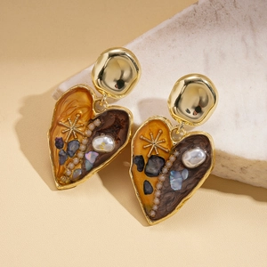 Detail view of gold heart drop earring with amber resin, pearl and gold star inlay