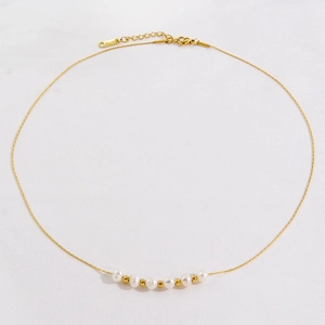 Elegant gold necklace with natural white pearls and stainless steel beads on white fabric