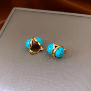 Detail of vintage round gold earrings featuring turquoise resin in a crisscross metal frame