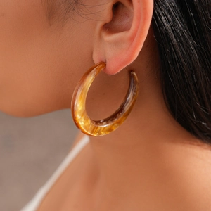 Close-up of a model wearing a thick amber resin C-shape hoop earring with marble pattern
