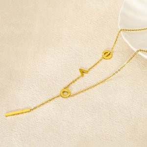 Detail of gold LOVE letter necklace with rectangular bar pendant on textured background