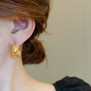 Close-up of gold U-shaped twisted hoop earrings worn by a model for a chic fashion look