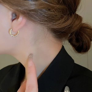Detail of elegant gold twisted hoop earrings with zircon studs worn on ear