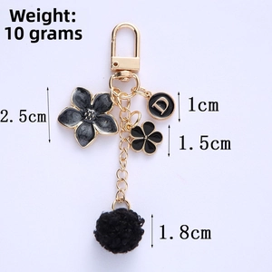 Detail of floral metal keychain with black pompom and letter D charm, weighing 10g