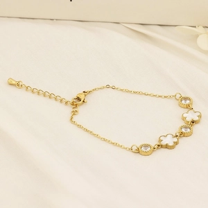 Detail of gold clover bracelet with white shells and crystal charms on silk