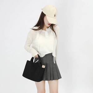 Detail of a black canvas tote bag with side pockets shown on a model in white background