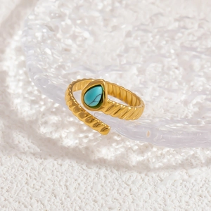 Close-up of gold stainless steel ring with turquoise stone on textured glass