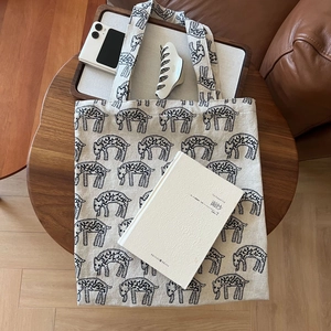 Flat lay of cream canvas tote bag with black animal print on a round wooden table