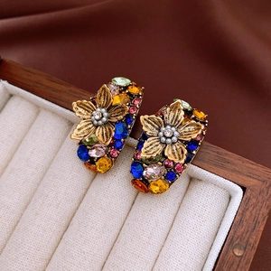 Close-up of vintage flower earrings with colorful rhinestones and pearls on beige velvet