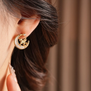 Close-up of golden vintage unicorn and moon stud earrings worn with elegant detail