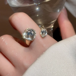 Detail of adjustable gold ring with square and drop-shaped zirconia on a silk background