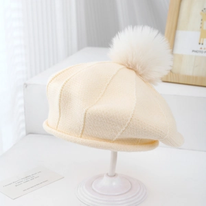 Détail d'un béret en tricot crème pour enfants avec un pompon moelleux et une maille côtelée